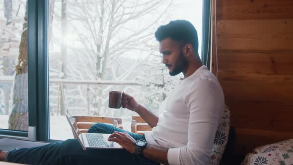 Young Man Relaxing Near the Window with Coffee and Browsing Social Media alt