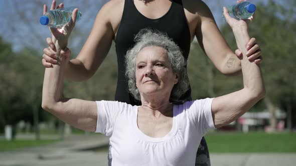 Fitness Trainer Teaching Senior Lady To Flex Hand Muscles alt