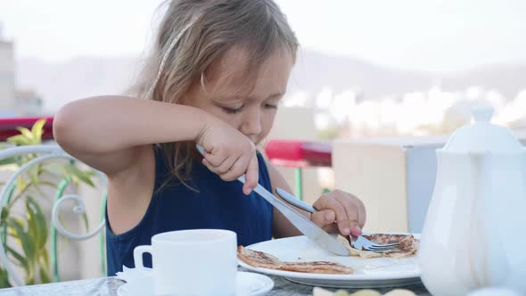 Portrait of Little Girl is Cutting a Pancake and Eating It for Breakfast