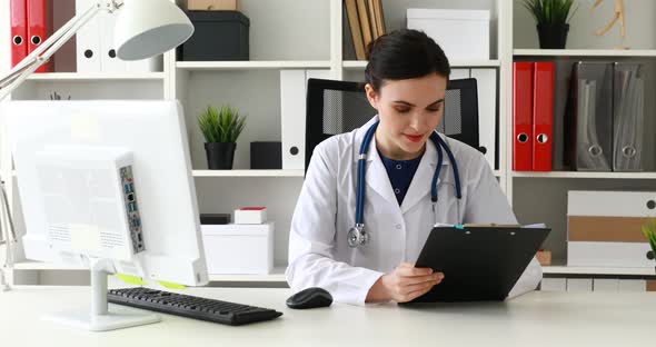Doctor in White Lab Coat Sitting at Workplace and Reading Documents
