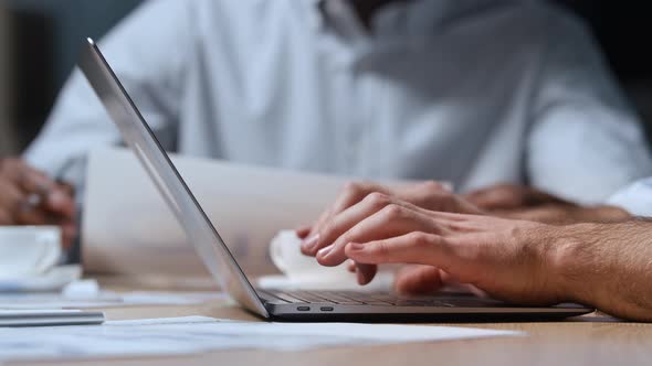 Side view of man typing on laptop keyboard while sitting at table in office alt