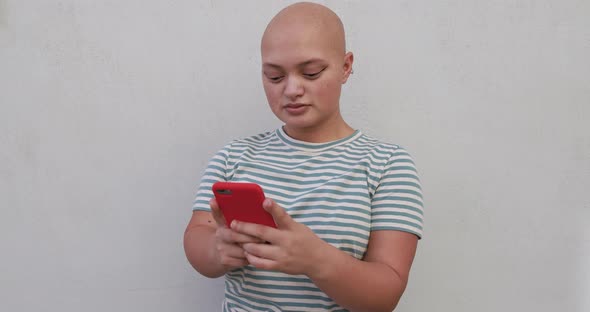 Bald girl using mobile phone in the city - Real people, diversity and technology concept alt