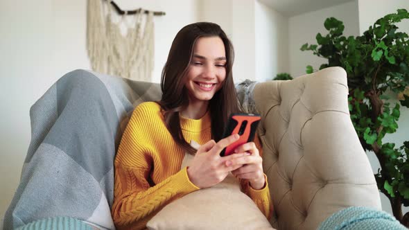 Woman Smiling Hold Smartphone Watching Social Media Stories Video Sit on Sofa alt