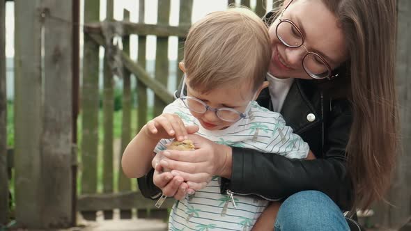 Child and Mother Holding a Chick in Hand in Backyard of Farm alt