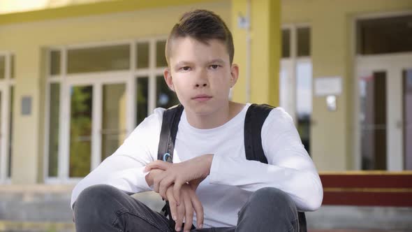 A Caucasian Teenage Boy Turns and Looks at the Camera As He Sits in Front of School  Closeup