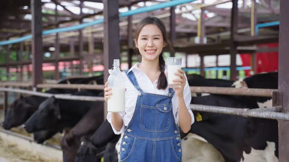 Portrait of Asian woman dairy farmer holding bottle of milk in cowshed alt