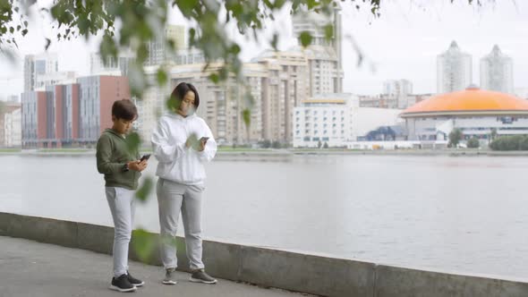 Asian Mother and Son Using Smartphone and Running Outdoors alt