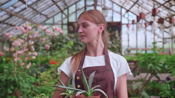 Young Blonde Girl Walks Through a Greenhouse with Pots of Flowers