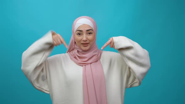 Excited Positive Young Muslim Woman in Hijab Pointing Fingers Down Asking to Subscribe or Like on