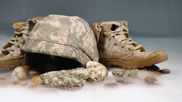 Boots And Military Helmets Piled On Rocks. alt