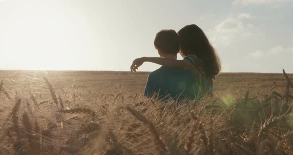 Boy and girl running in a golden wheat field together towards the sunset alt