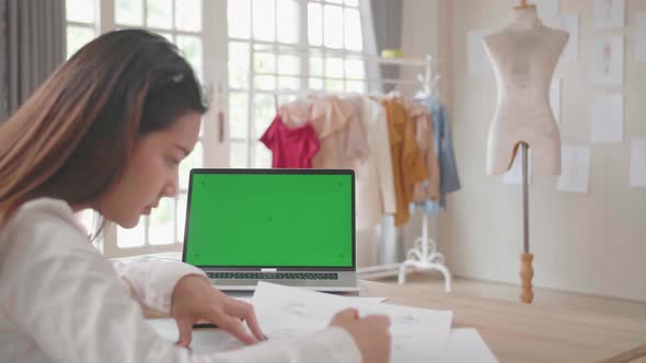 Asian Female Designer Sketching On Paper With Green Screen Laptop Display alt