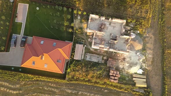 Top Down Aerial View of Two Private Houses One Under Construction with Wooden Roofing Frame and alt