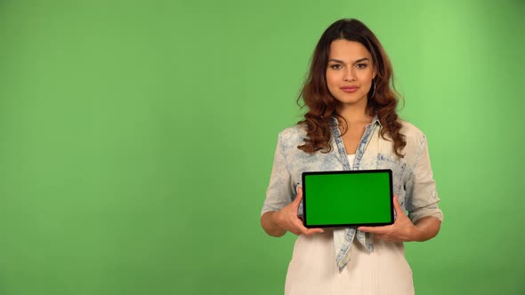 A Young Caucasian Woman Shows a Tablet with Green Screen to the Camera with a Smile  Green Screen