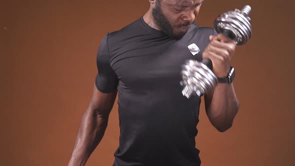 A Darkskinned Man Lifts Dumbbells on an Isolated Dark Background