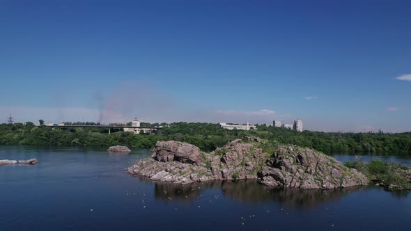 Rocky island and a flock of seagulls in the middle of the river, wild nature among modern city.