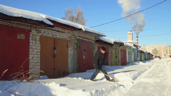 A Man with a Shovel Carefully Clears the Snow From the Road Outside His Garage alt