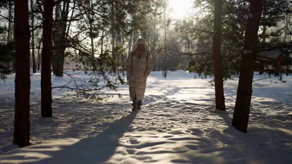 A Man in Warm Winter Clothes Walks Through a Winter Forest on a Sunny Day alt