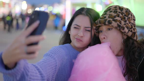 Lovely Female Couple Shoot Selfies with Phone Eating Candy Floss and Making Funny Faces in Amusement alt