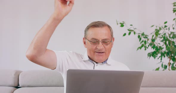 An Elderly Man with a Laptop Computer Cheers Upon Reading Good News alt