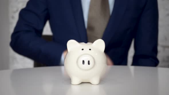 Business Man Putting Coins in White Piggy Bank Indoors  Business Money Saving and Finance Concept alt