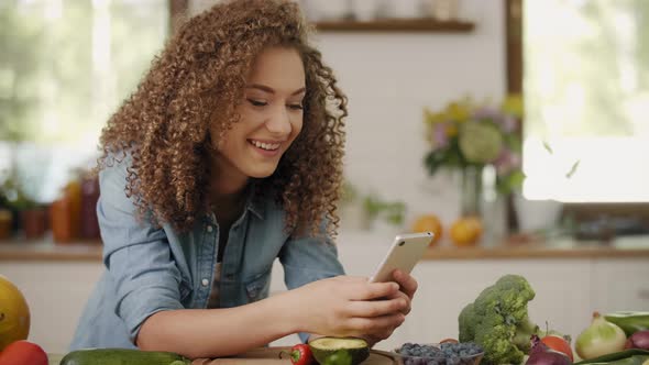 Handheld view of young woman with mobile phone in the kitchen alt