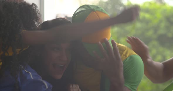 Brazilian football fans celebrating victory while watching televised match at home, slow motion