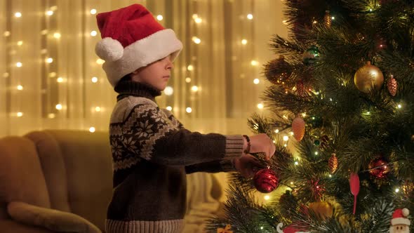 Happy Smiling Boy Decorating Christmas Tree with Red Bauble alt