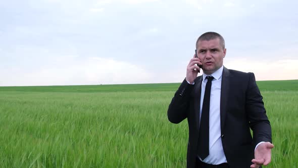 Angry Businessman Talking on a Smartphone in the Middle of the Field alt