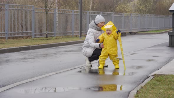 Mother with Small Cute Child in Yellow Waterproof Rain Pants Raincoat and Rubber Boots for Kids alt