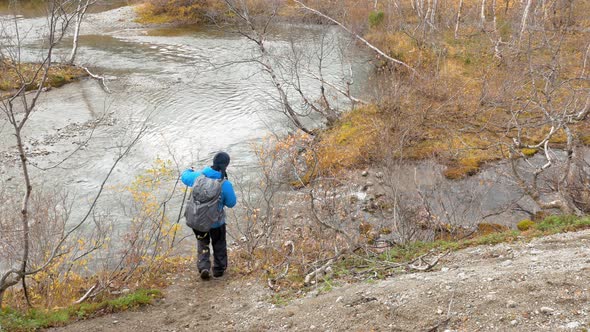 Traveler with a Backpack Is on the Trail. He Approaches the Mountain Stream alt