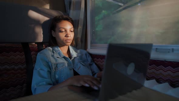 African Female Freelancer Working at a Laptop While Sitting in a Car Typing Text and Remote Work in alt