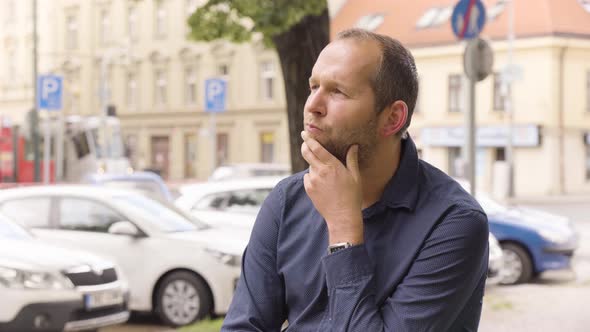 A Caucasian Man Thinks About Something in an Urban Area  a Colorful Street in the Blurry Background