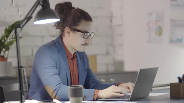 Quirky Entrepreneur Working on Laptop Late at Night in Office alt