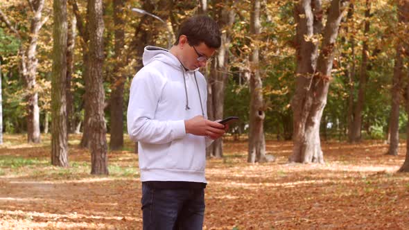 Young Man Using Smartphone In Autumn Park