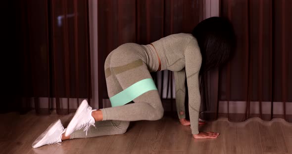 Athletic African American beautiful woman doing squat side kick using a fitness elastic band.