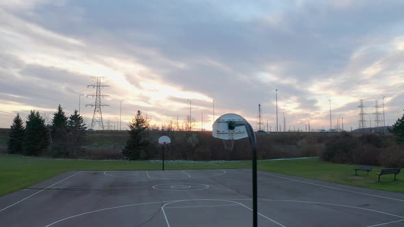 Sun setting behind a basketball net and vehicles driving past on a nearby highway with large utility alt