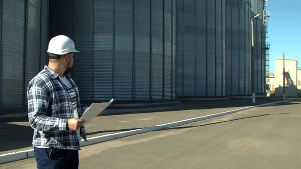 Professional Engineer with Blueprints Inspecting Agricultural Silos