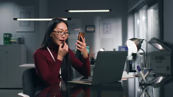 Businesswoman Apply Lipstick at Desk in Modern Office alt