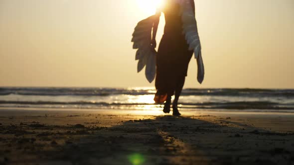 Silhouette of Beautiful Female Angel Walking Barefoot Toward the Sea at Sunset