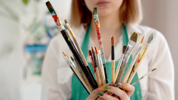 Female Artist in an Apron Holds Lot of Brushes in Hands Closeup alt
