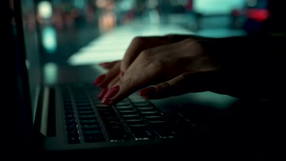 A Woman Works on a Laptop at Home on a Blurred Background of a Working TV alt