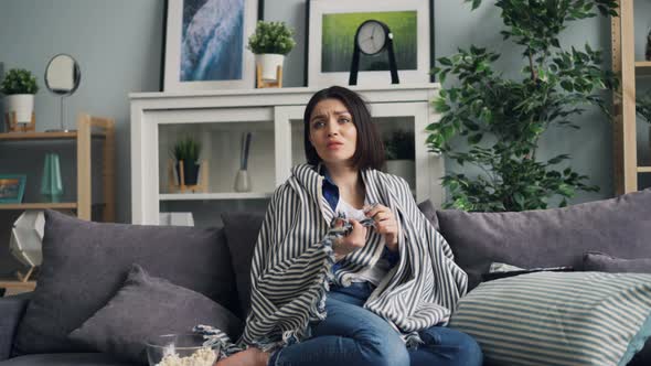 Zoom-in of Young Woman Watching Scary Thriller on TV Sitting on Sofa at Home alt