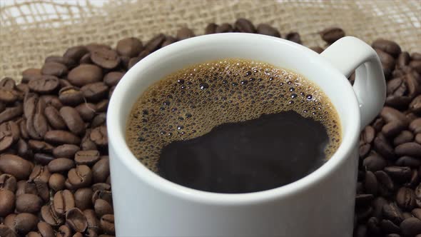White Cup with Coffee on the Background of Fresh Roasted Coffee Beans