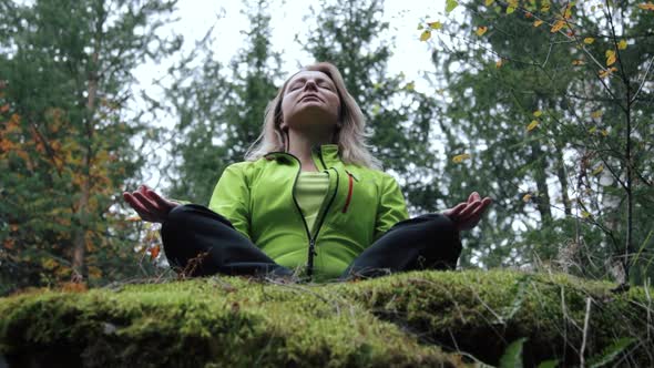 Woman meditating on a rock in the forest