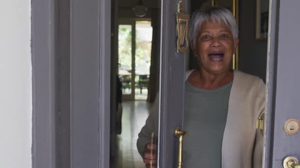Smiling senior mixed race woman opening front door and welcoming alt
