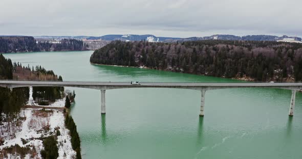 Quadcopter Video of a Bridge Across a River to Hills Covered in Snowy Forest
