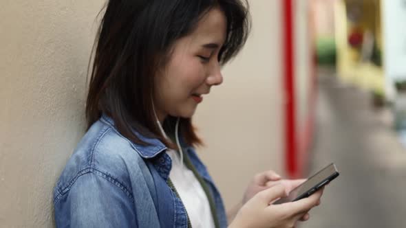 Smile of Asian woman using smartphone scrolling new feed social media at a small street.