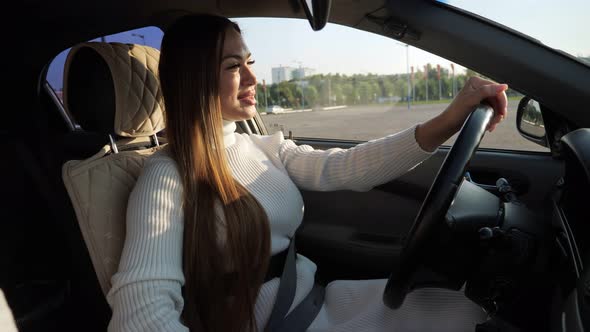 Smiling Young Woman Holds Hand on Leather Steering Wheel alt