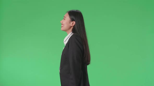Side View Of A Smiling Asian Business Woman Walking Through Green Screen In The Studio alt